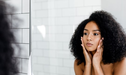 Femme se regardant dans le mirroir pour constater les effets du CBD contre l'acné
