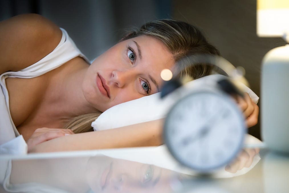 Une femme dans son lit regardant son reveil pour symbolier les effets du CBD sur les troubles du sommeil