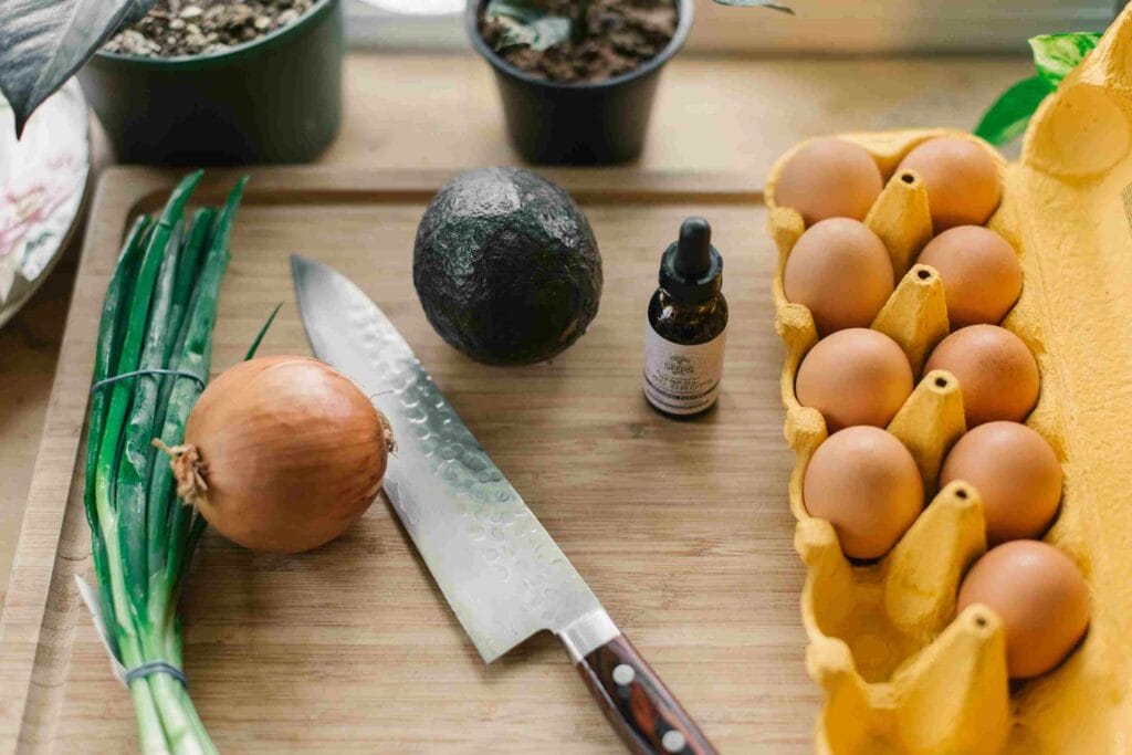 Des aliments frais et un couteau bien aiguisé sur une planche en bois à côté d'une bouteille d'huile de chanvre.