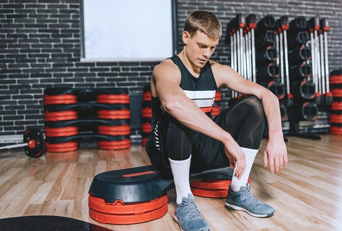 Ein Mann sitzt auf einem Sportgerät, das die Wirkung von CBD auf die Erholung beim Sport symbolisiert.