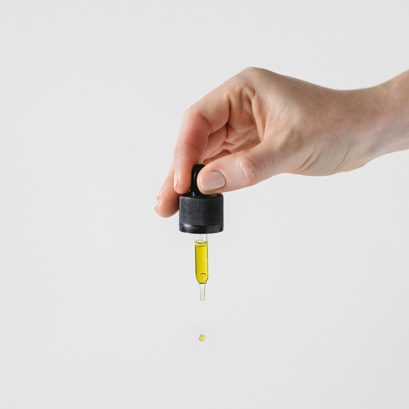Main tenant une pipette de CBD avec une goutte d'huile de CBD tombant, sur fond blanc