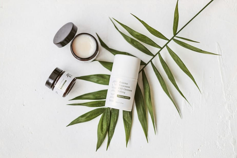 Produits topiques au CBD sur une feuille verte, comprenant des pots de crème et un tube de pommade pour le traitement de l'eczéma