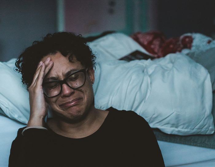 Person in emotionaler Not, die am Boden sitzt und ihren Kopf mit einem Ausdruck intensiver Traurigkeit hält