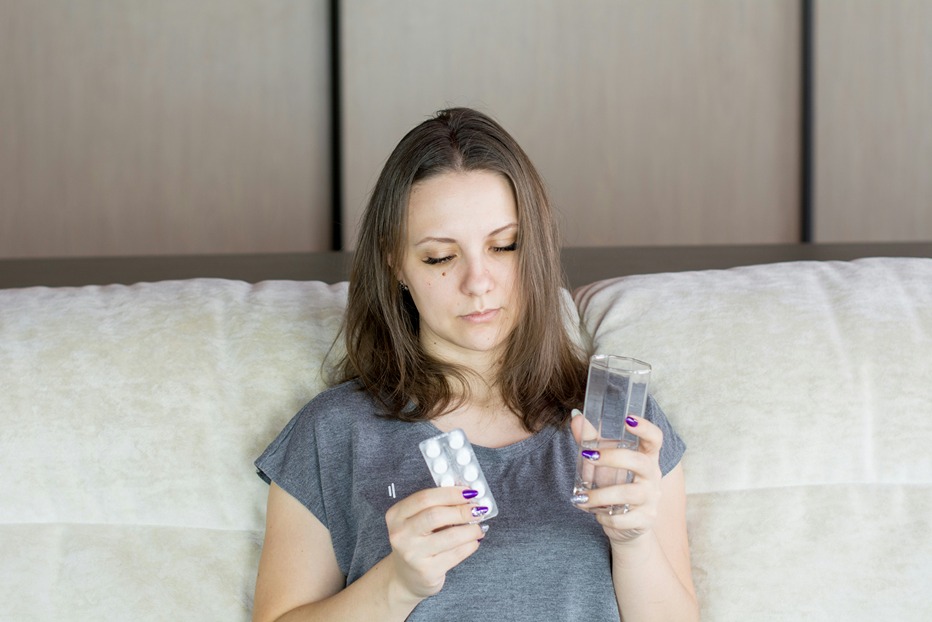Femme regardant des comprimés avant prise, illustrant les interactions possibles entre CBD et analgésiques